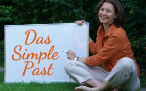 Frau sitzt im Gras und hält ein Flipchart. Darauf steht: Das simple past.